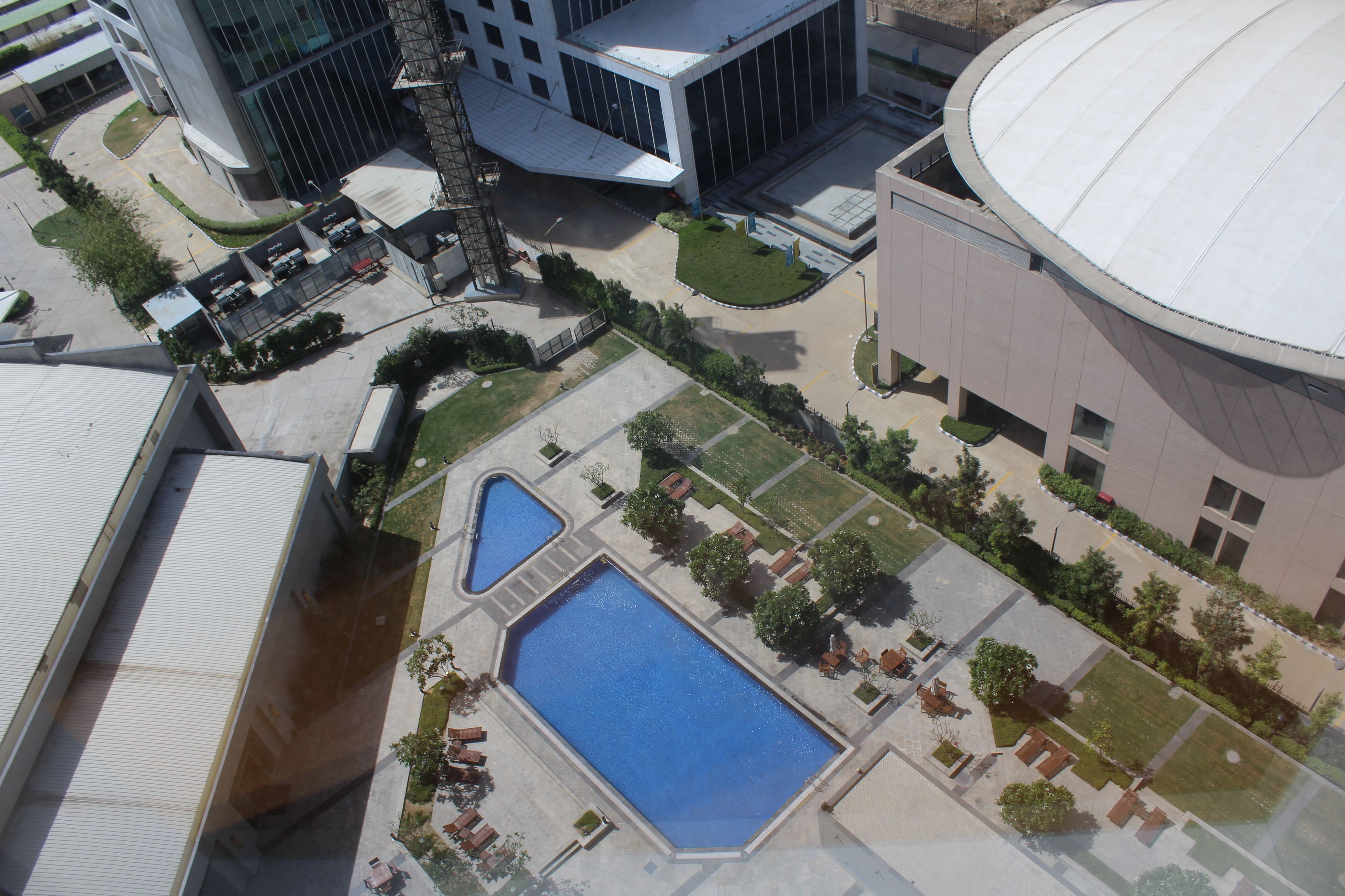 An aerial view of a modern building complex with multiple pools, landscaped areas, and a large circular structure.