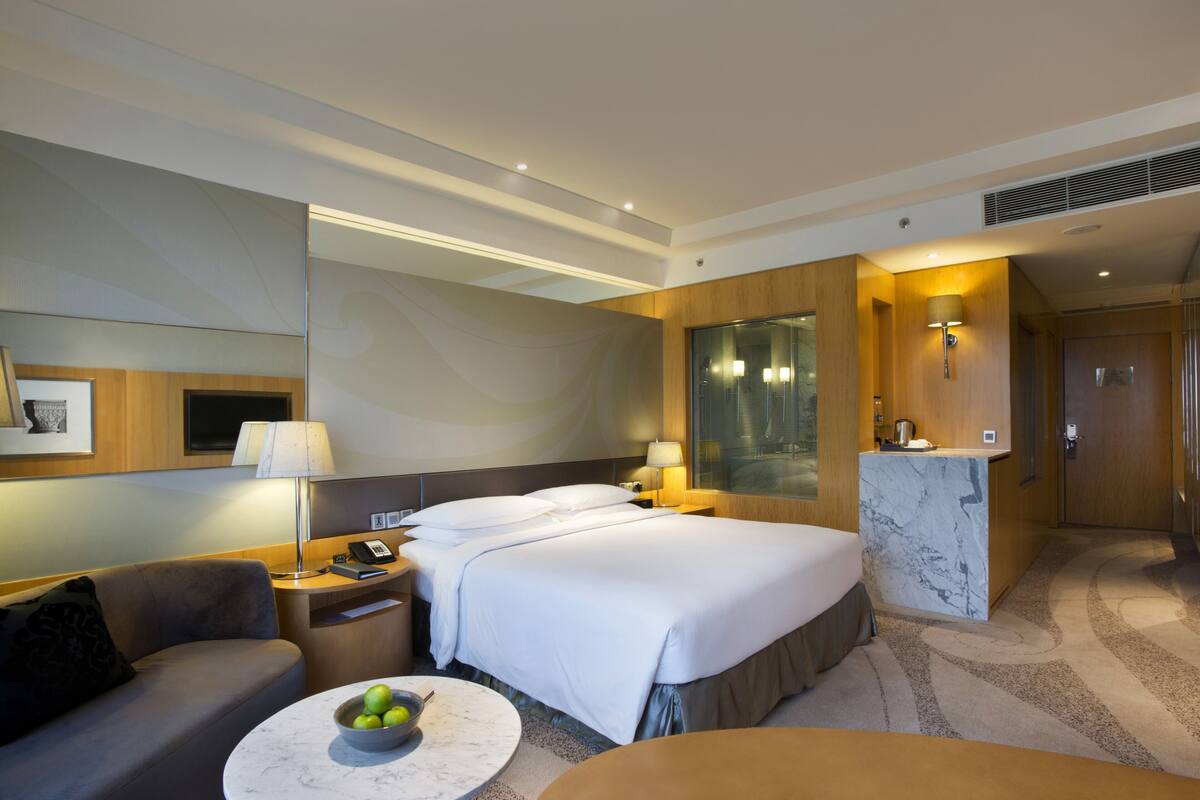 Habitación de hotel con cama, escritorio, silla, sofá y una mesita con fruta.