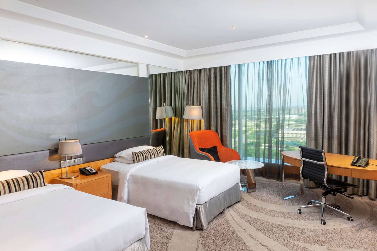 Habitación de hotel con dos camas, un escritorio, una silla y vistas a la ciudad.