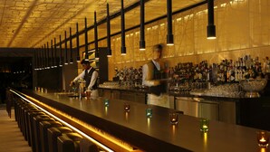 Een bar met een lange toonbank, verschillende krukken en een goed gevulde bar.