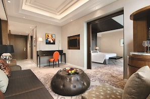 Una habitación de hotel moderna con una cama grande, una zona de estar con una mesa de centro, un escritorio y un televisor.