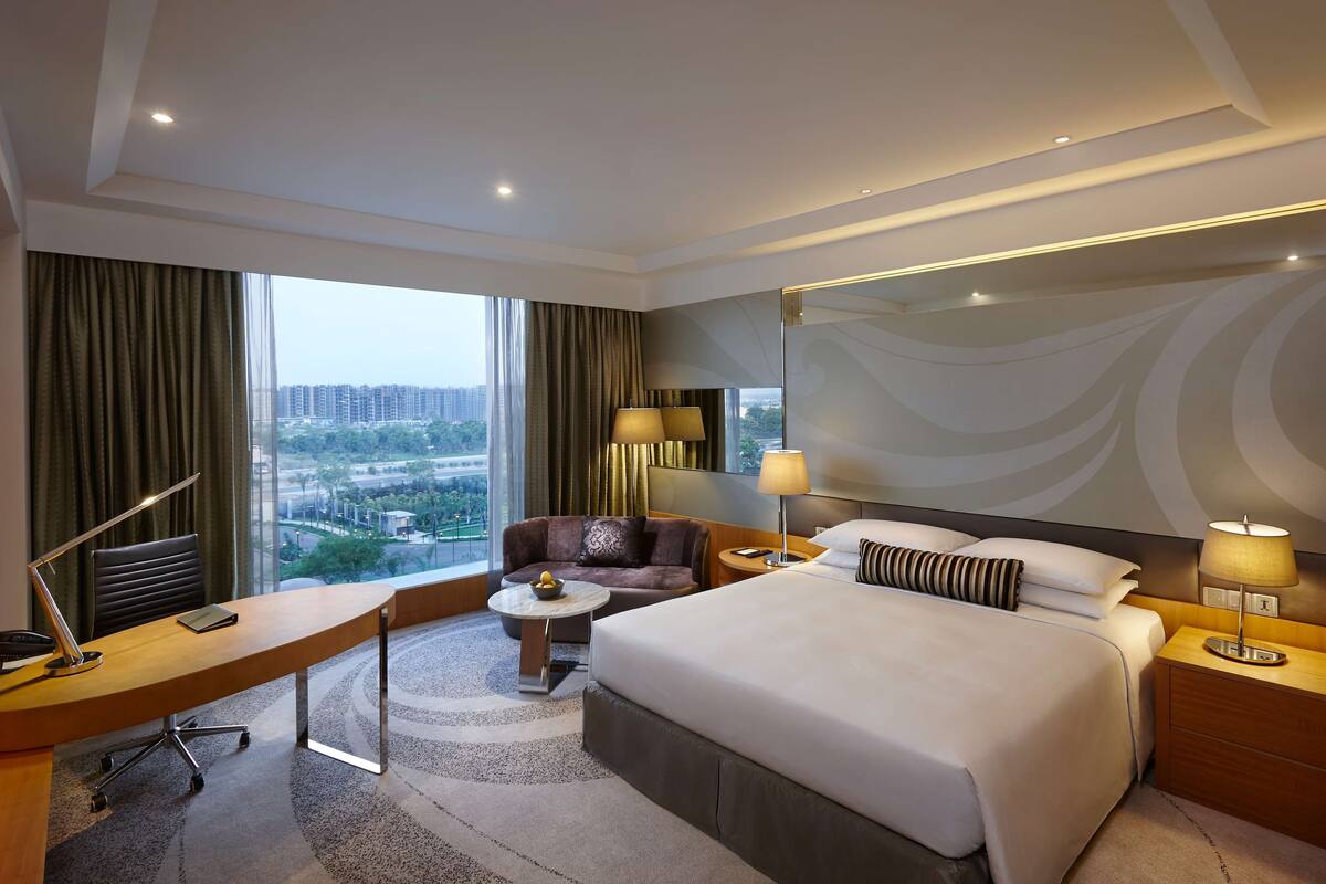 Habitación de hotel con una cama grande, un escritorio, una silla, una mesita y vistas a la ciudad.