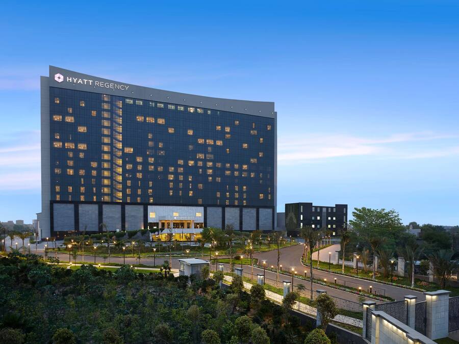 Un moderno hotel Hyatt Regency con una amplia fachada de vidrio, varios pisos y un área exterior bien cuidada con senderos y jardines.