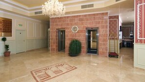 A spacious lobby with a marble floor, a chandelier, a reception desk, and a potted plant. - Mena Palace (Sunny Beach)