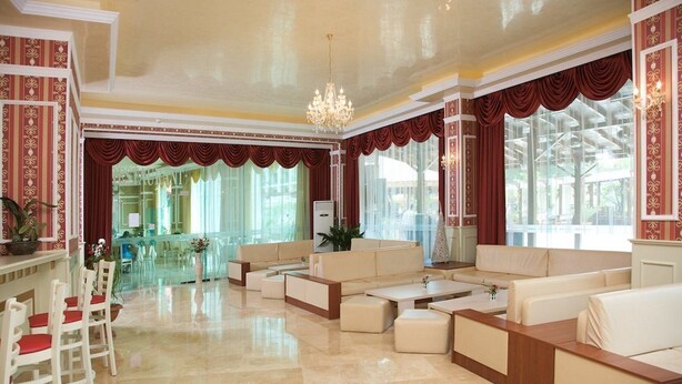 A spacious lobby with a large seating area, a chandelier, and a view of the outdoor area. - Mena Palace (Sunny Beach)