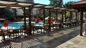 An outdoor poolside area with tables and chairs, umbrellas, and a pool. - Mena Palace (Sunny Beach)
