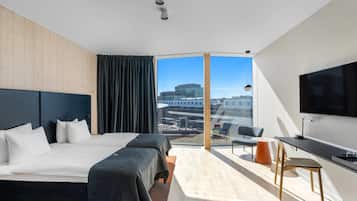 A modern hotel room with a large bed, a desk, a chair, and a TV.