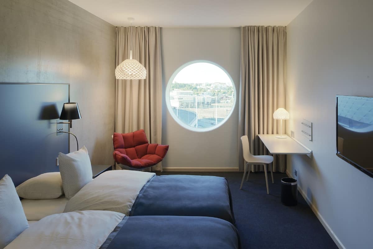 Ein Hotelzimmer mit zwei Betten, einem Schreibtisch, einem Stuhl, einem runden Fenster und einem Fernseher.