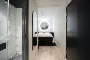 Un baño moderno con ducha, espejo y cama con mesita de noche.
