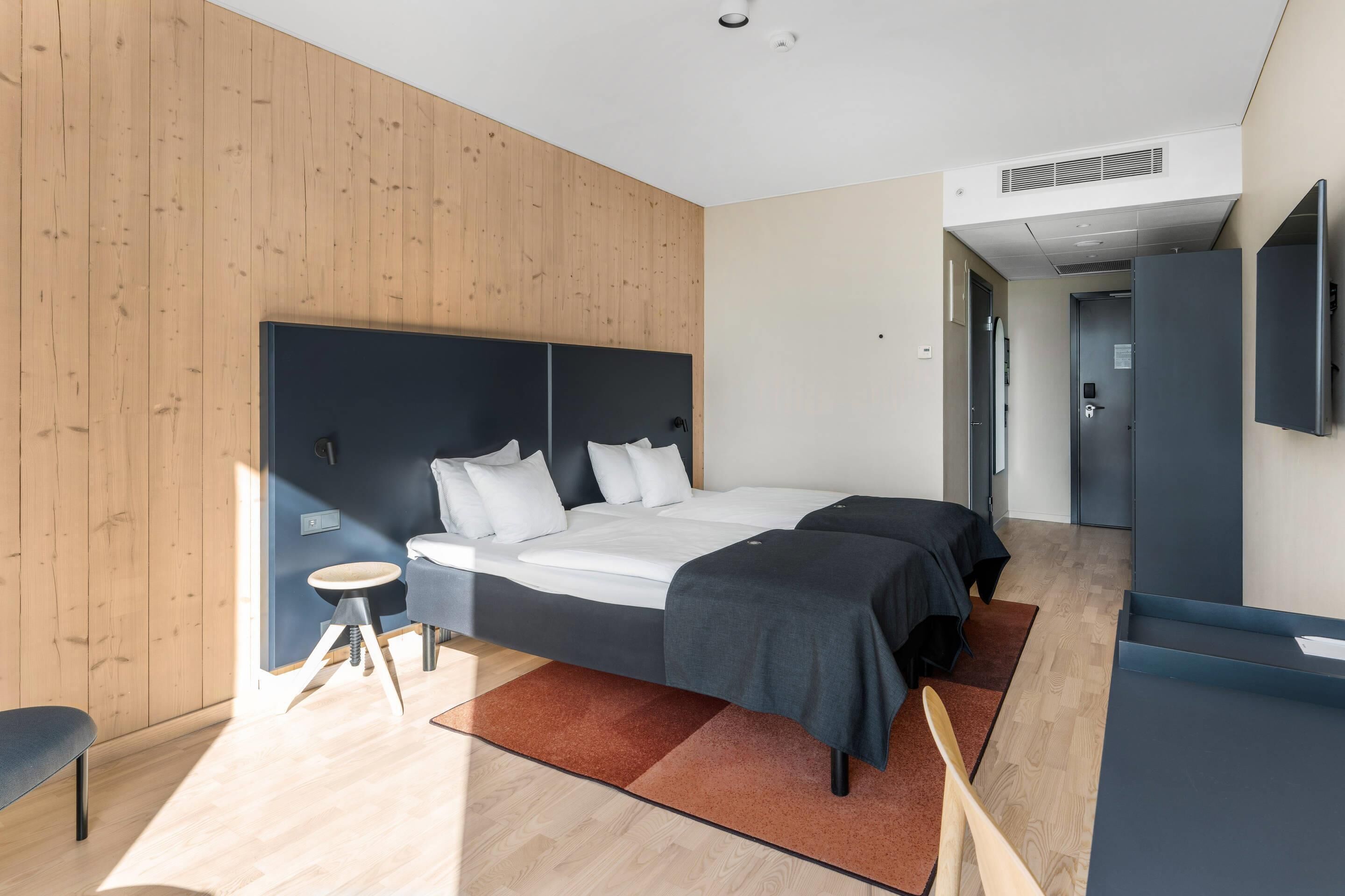 Una habitación de hotel moderna con una cama grande, un escritorio y un televisor de pantalla plana.