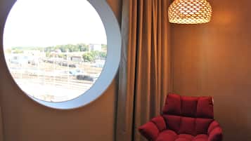Una habitación con ventanal circular, una silla roja y una lámpara colgante.