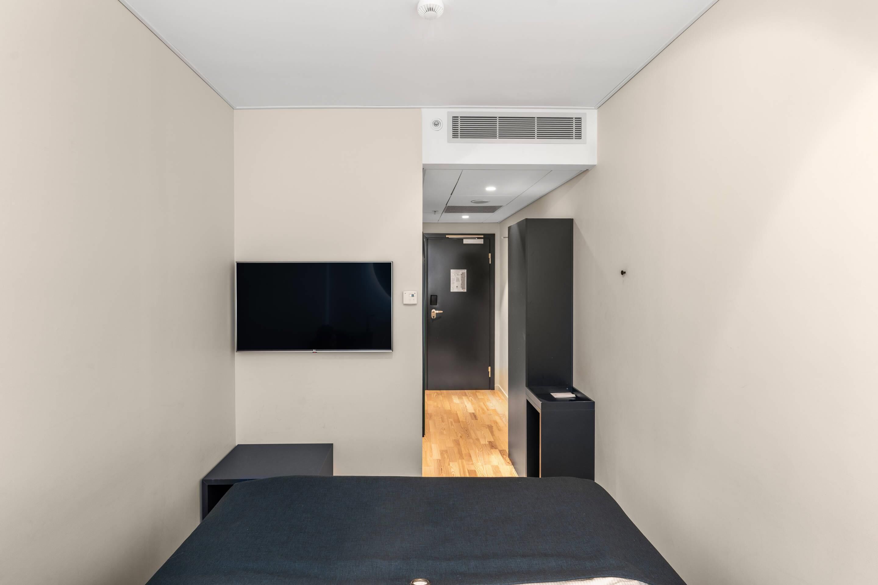 A modern hotel room with a bed, a flat-screen TV, a wardrobe, and an air conditioning unit.