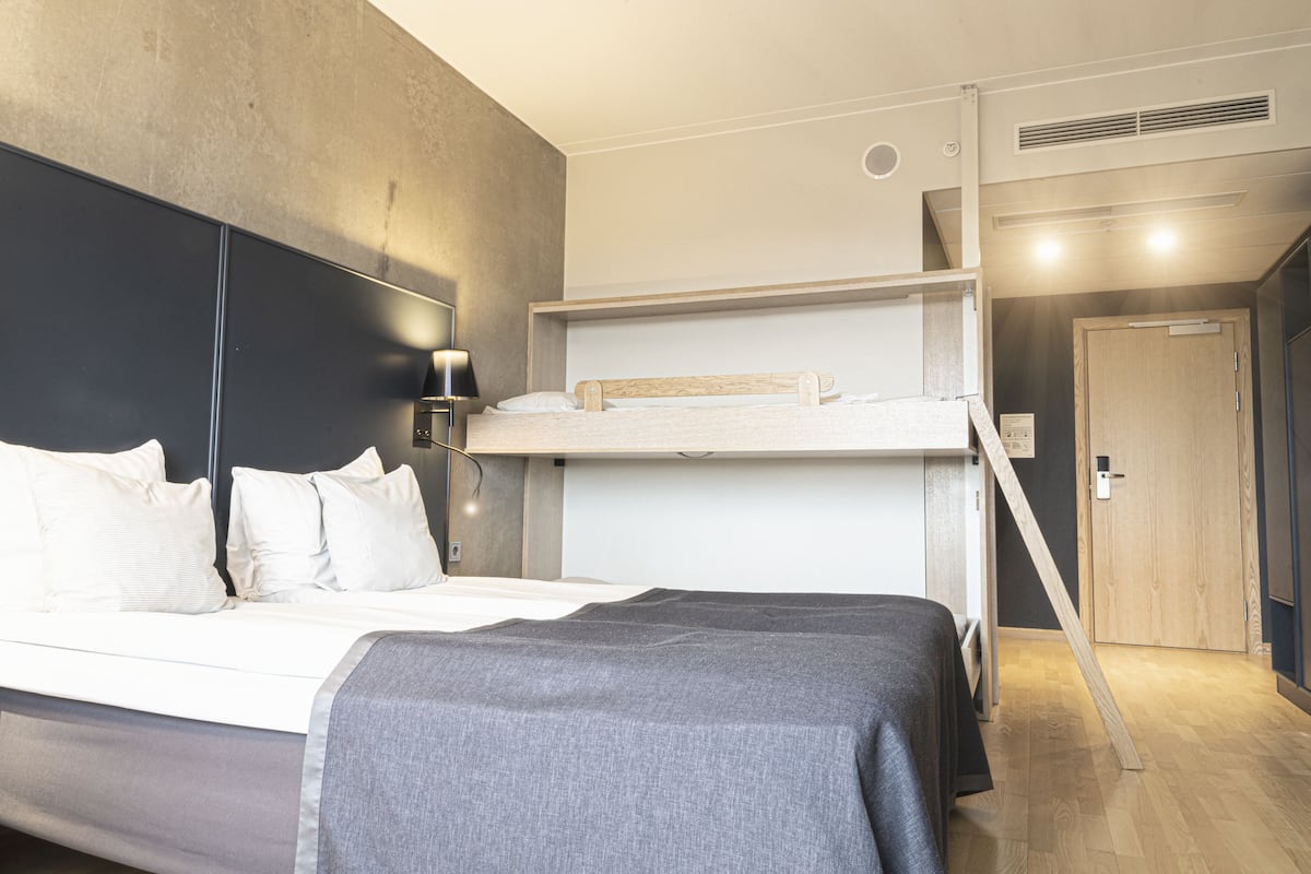Ein modernes Hotelzimmer mit einem Stockbett, einem großen Bett und einem Nachttisch mit Lampe.