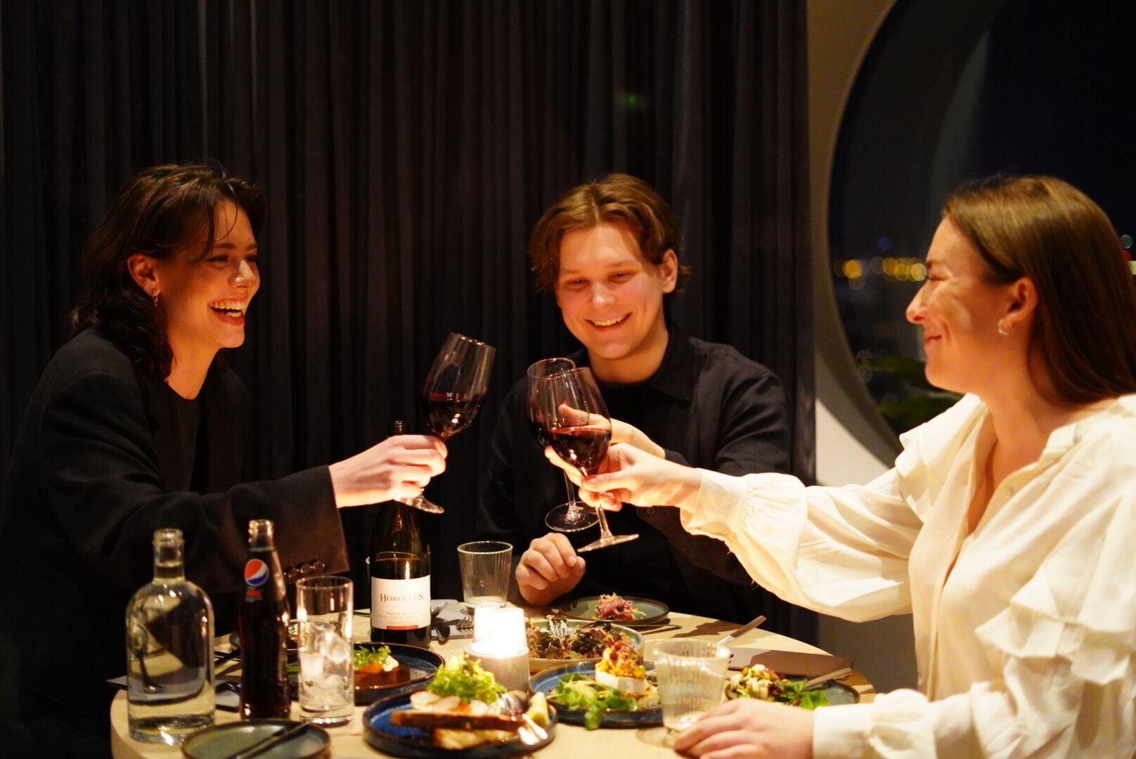 Un grupo de personas brindando con copas de vino en una mesa de cena con diversos platos y bebidas.
