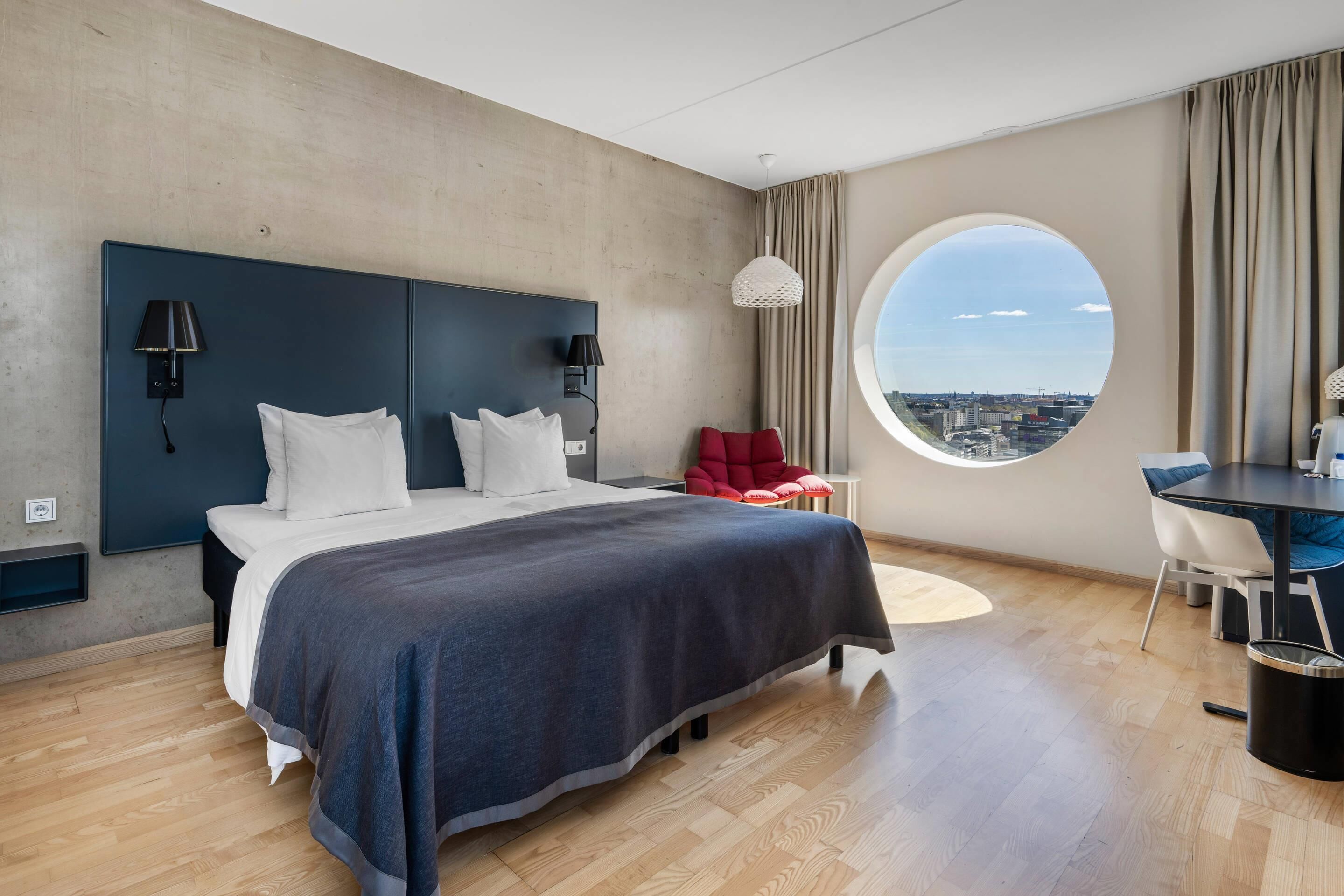 A modern hotel room with a large bed, a desk, and a view of the city.