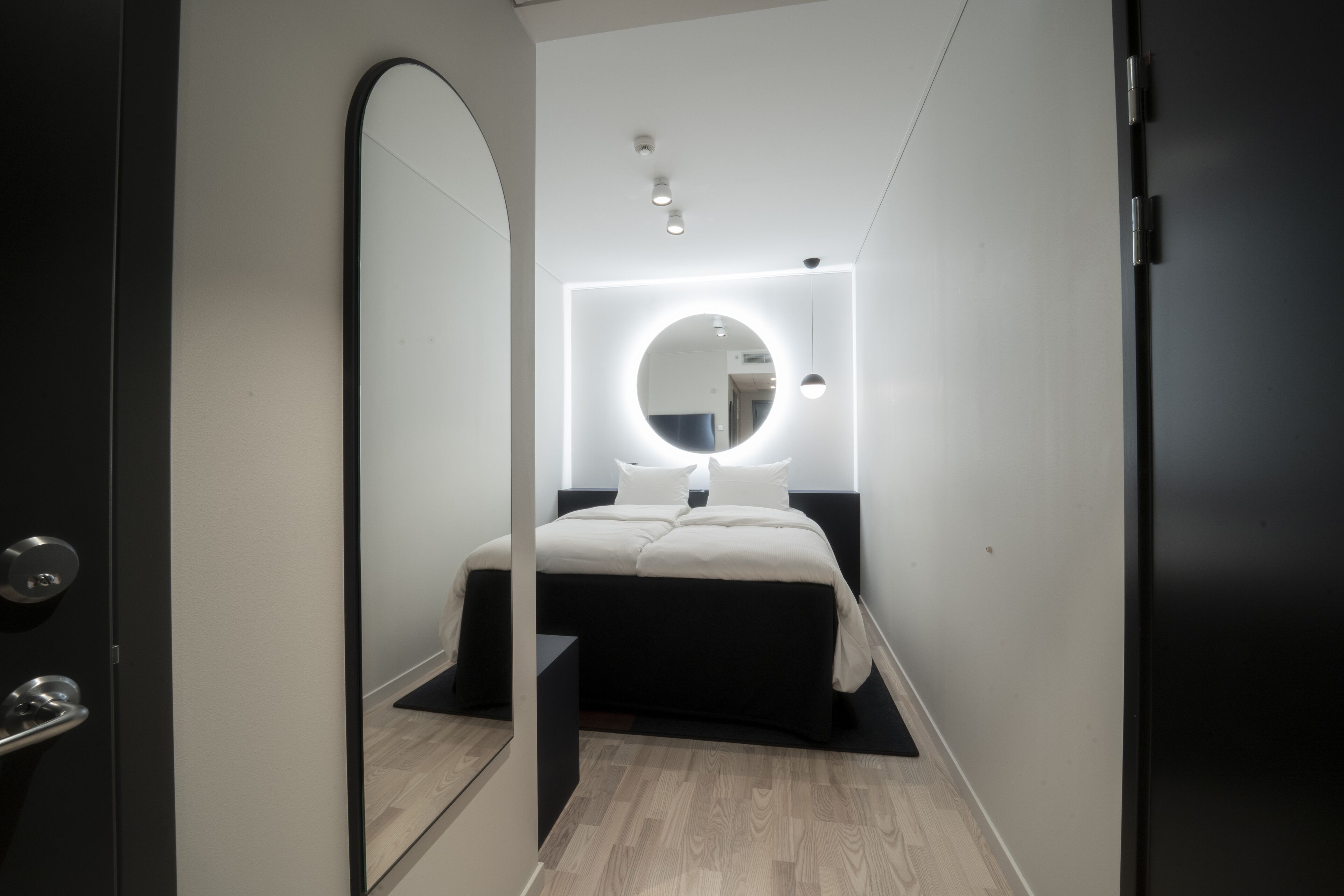 A modern bedroom with a large mirror, bedside table, and a neatly made bed.