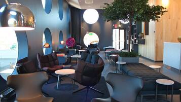 A modern lounge area with sofas, chairs, and tables, featuring a large tree and a circular light fixture.