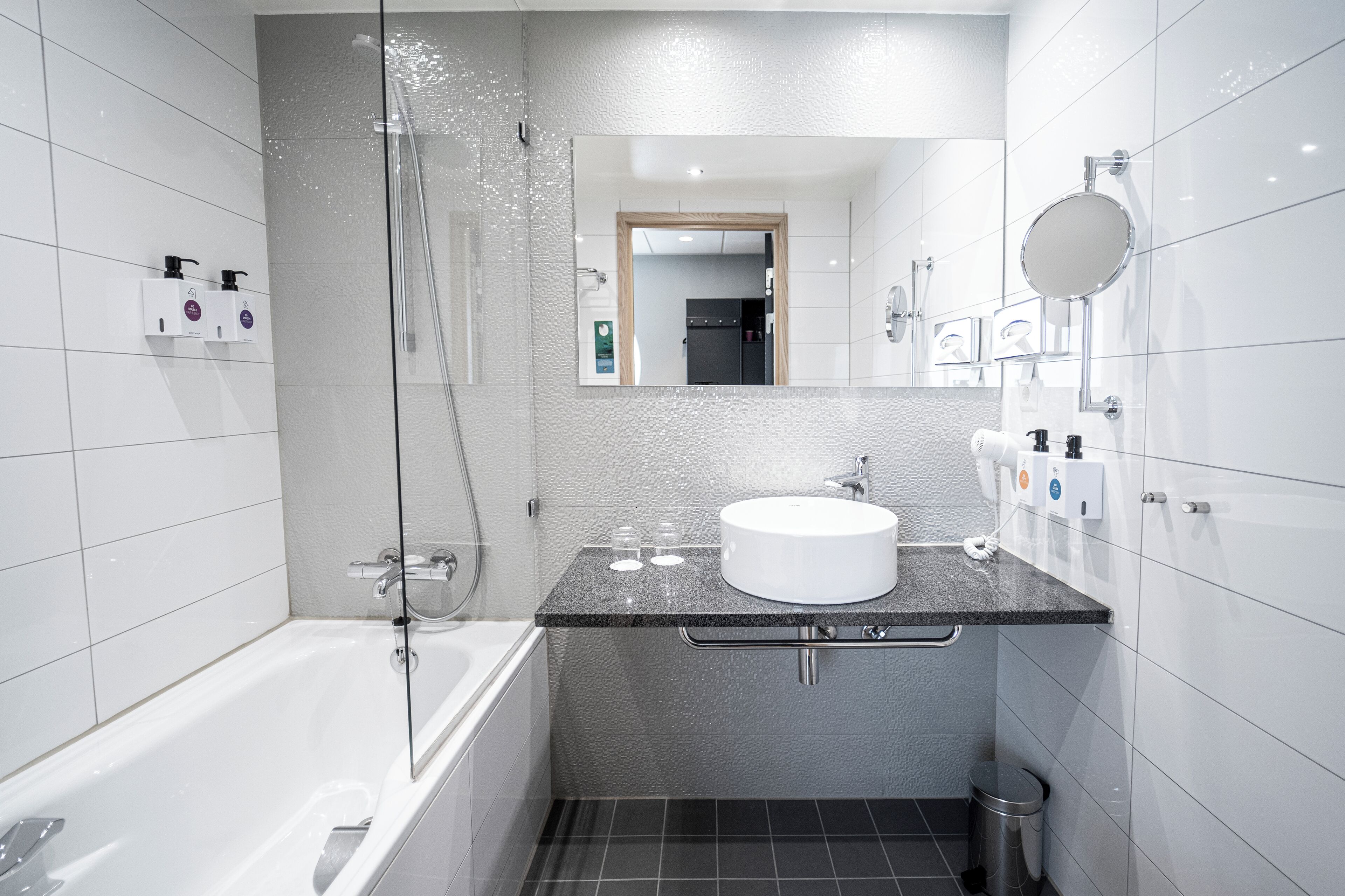 A modern bathroom with a glass-enclosed shower, a white bathtub, and a granite countertop sink.