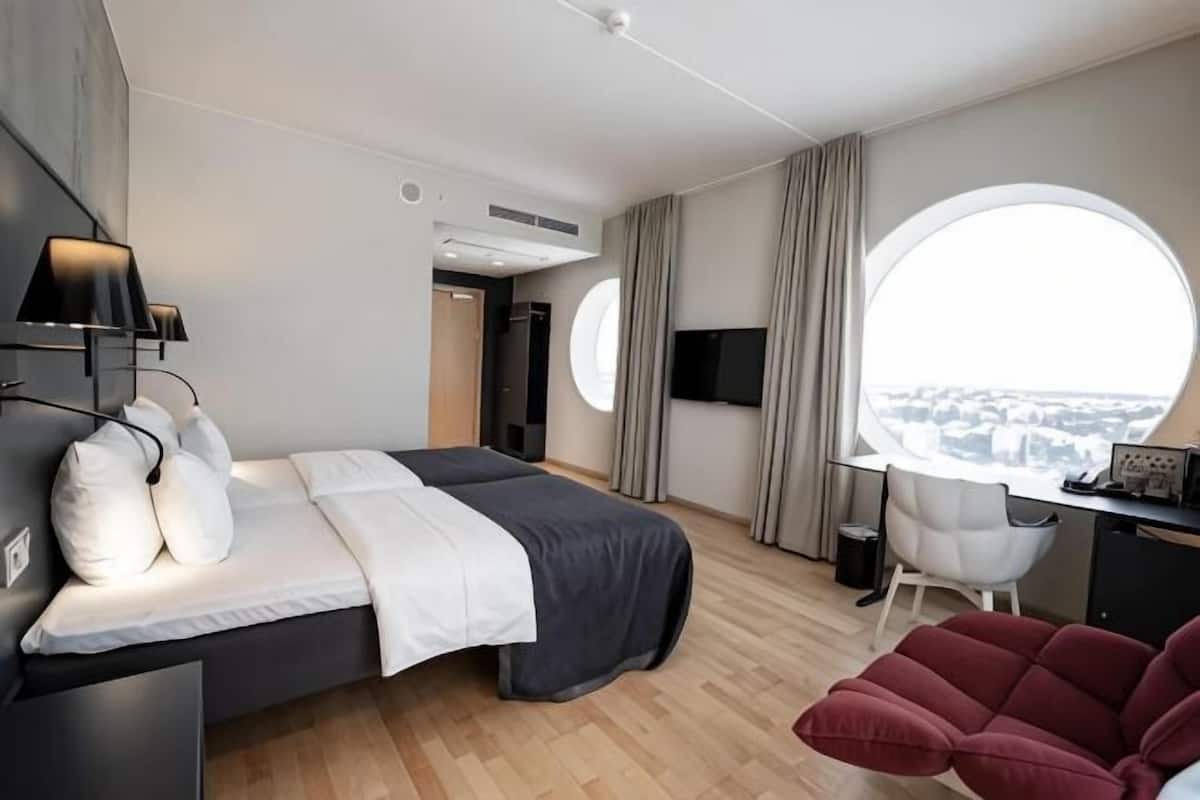 Ein modernes Hotelzimmer mit Bett, Schreibtisch, Stuhl und großem Fenster mit Blick auf die Stadt.