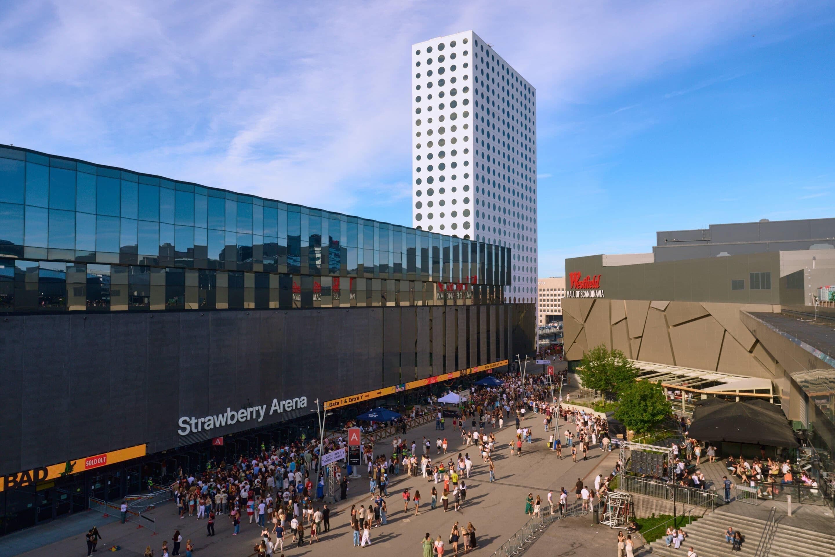 A modern building with a glass facade and a large crowd in front.