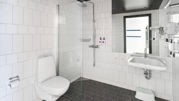 Ein modernes Badezimmer mit weißen Fliesen, einer Dusche, einer Toilette, einem Waschbecken und einem Spiegel.