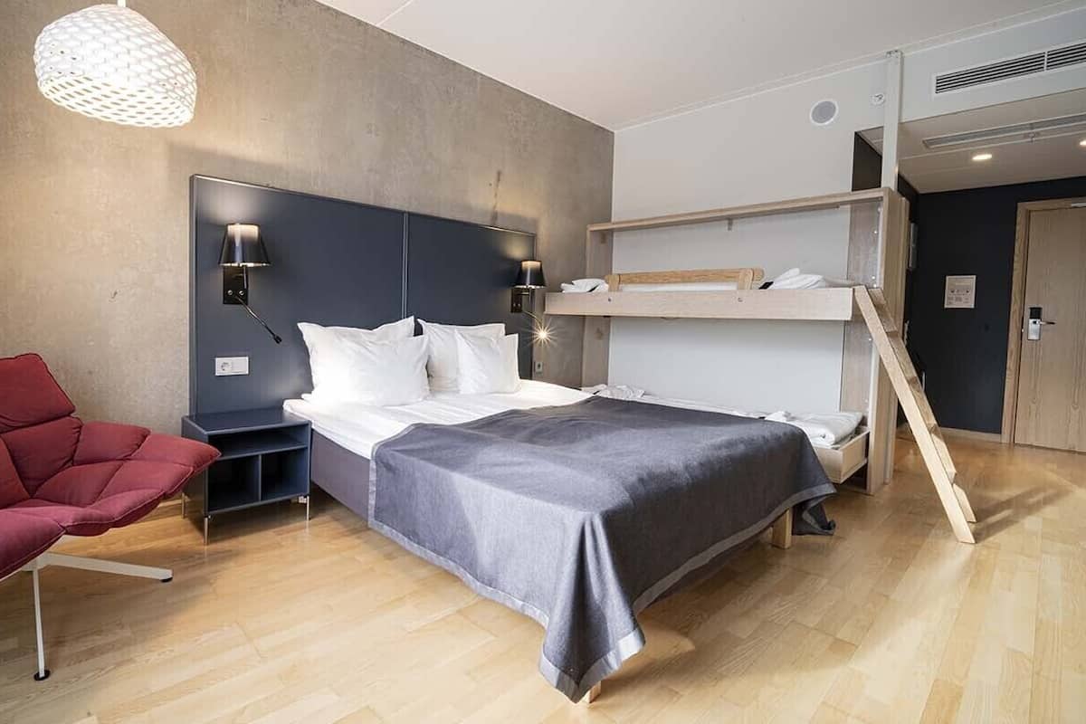 Ein modernes Hotelzimmer mit Etagenbett, einem roten Sessel, einem Nachttisch und einer Pendelleuchte.