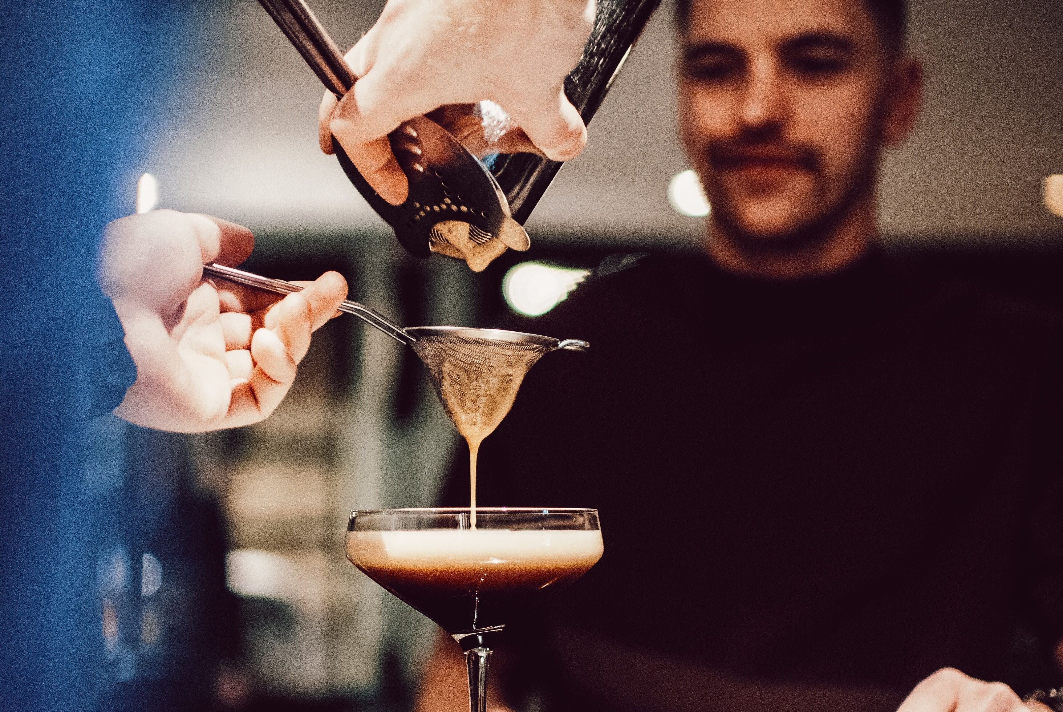 A person pouring a drink into a martini glass.