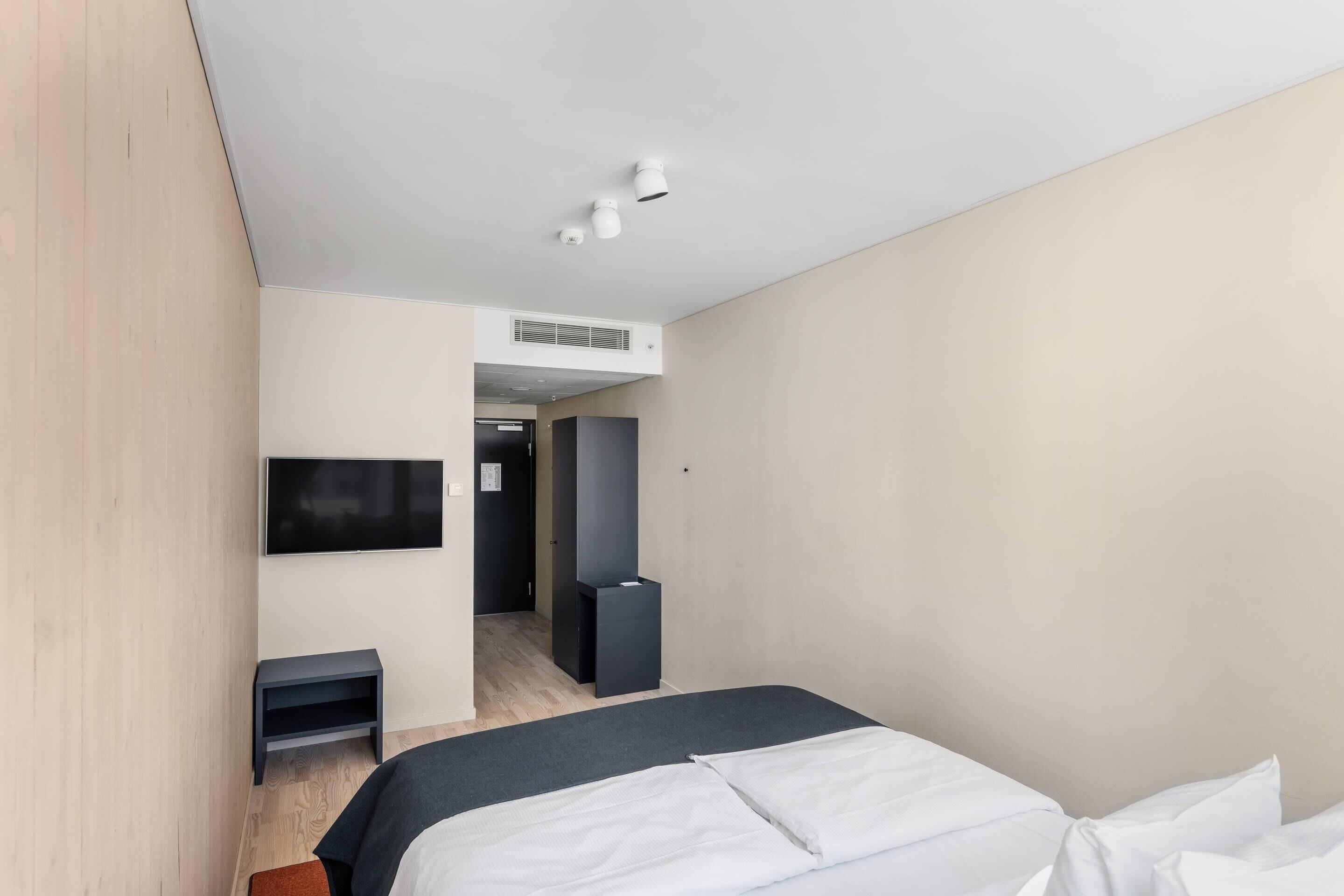 Una habitación de hotel moderna con una cama, televisión, escritorio y armario.