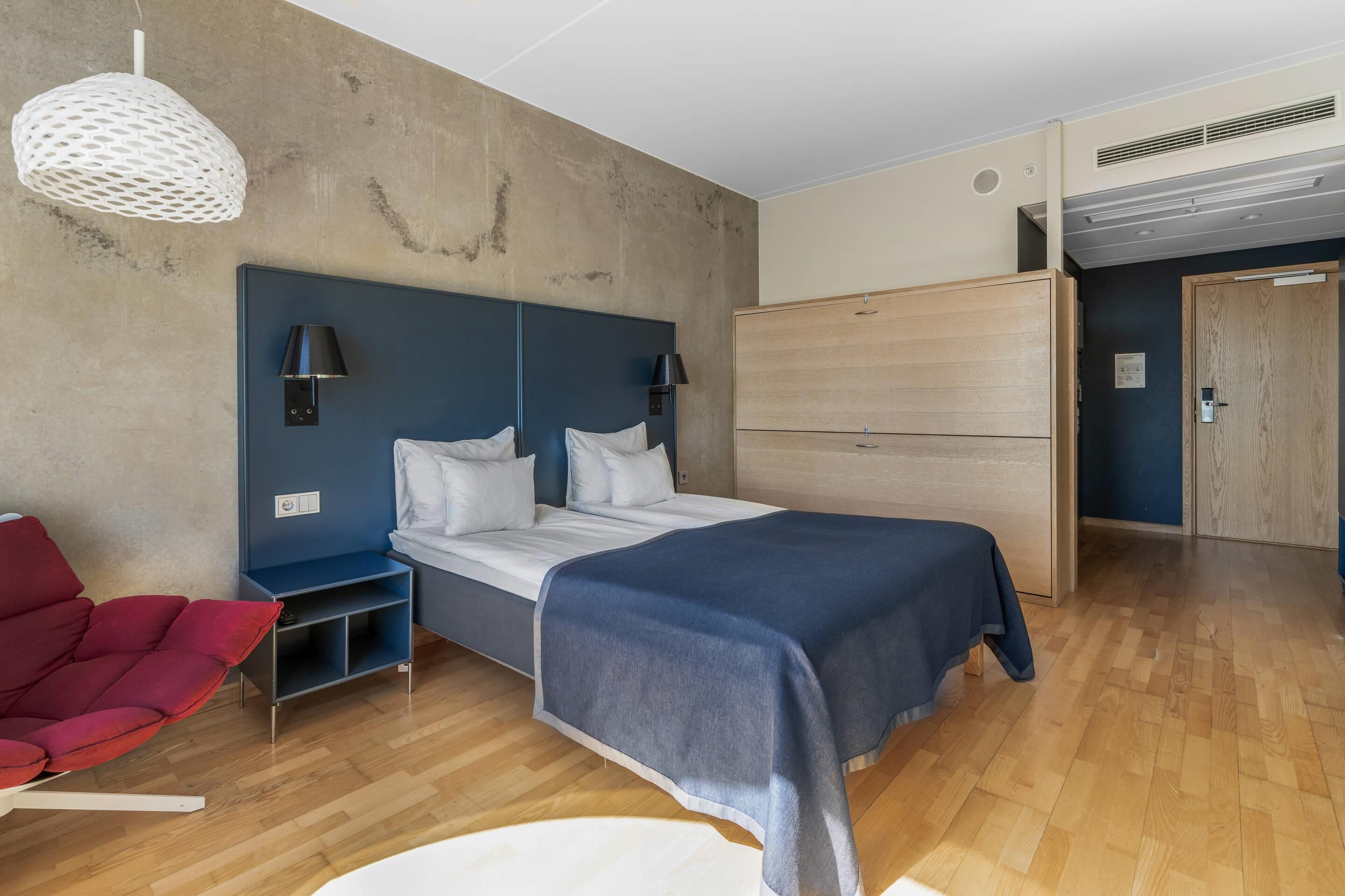 Een moderne slaapkamer met een bed, nachtkastjes, een rode stoel en een kledingkast.