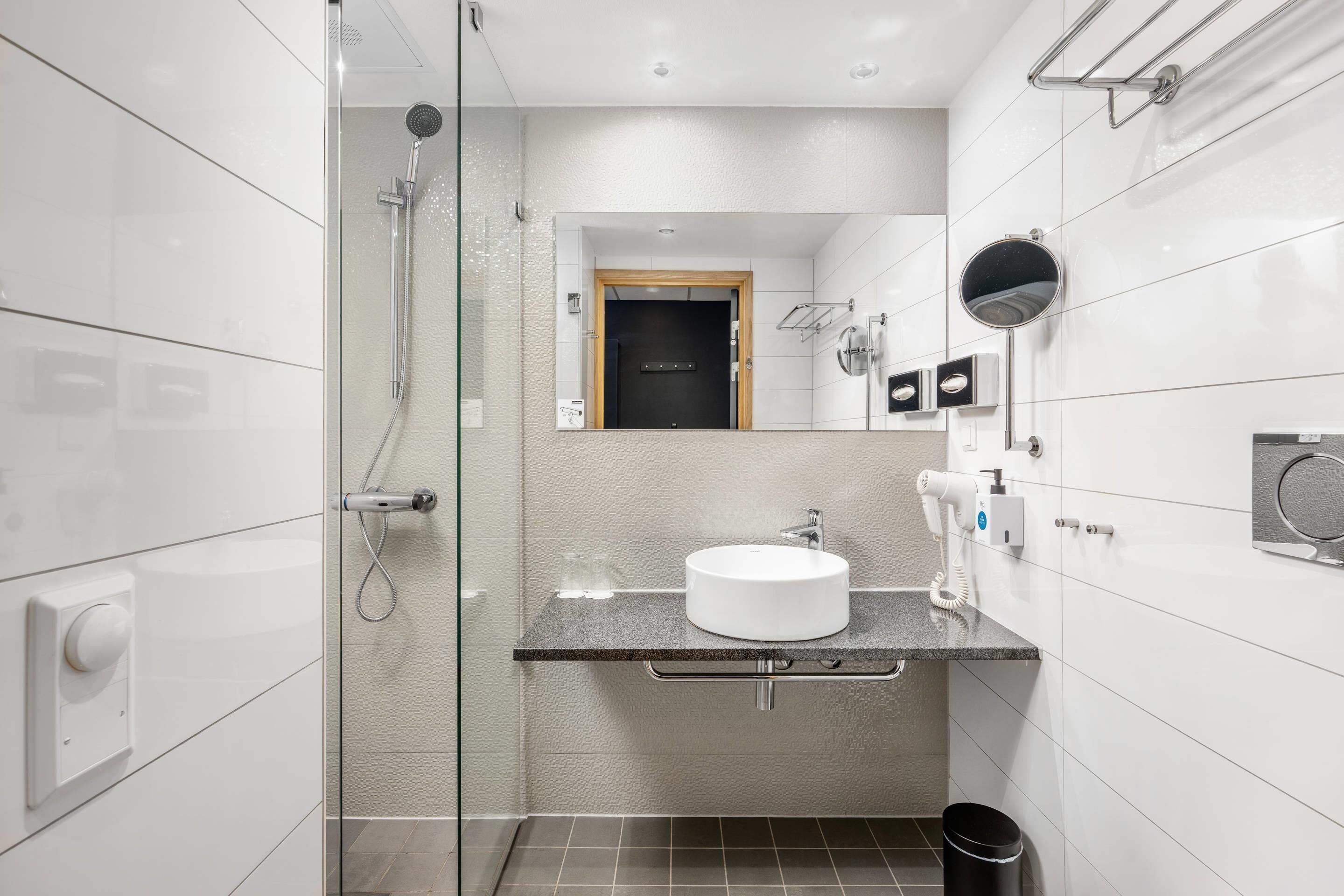 Ein modernes Badezimmer mit einer gläsernen Duschkabine, einem Waschbecken mit Spiegel und einem Föhn.