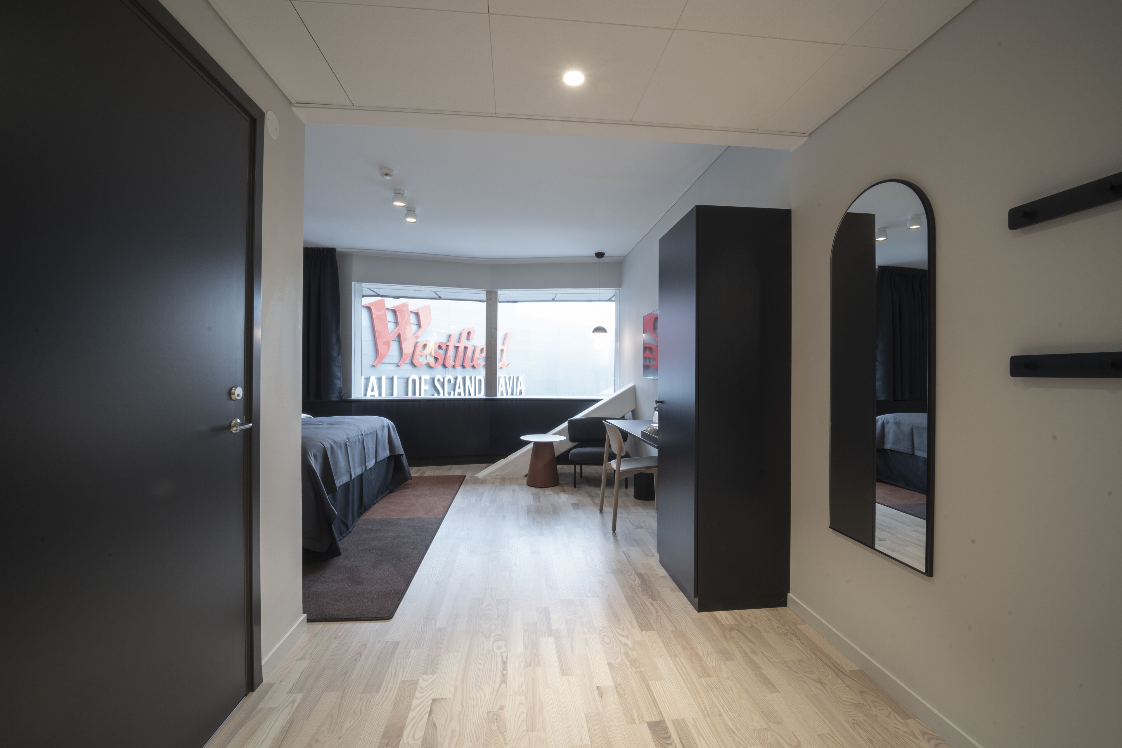 A modern hotel room with a bed, desk, and large window.