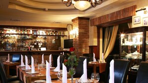 A restaurant with wooden tables set for dining, a bar area with bottles, and a chandelier. - Old Continent Hotel (Uzhhorod)