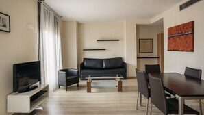 A modern living room with a flat-screen TV, a black leather sofa, a glass coffee table, and a dining table with chairs. - Villarroel Apartments Barcelona (Barcelona)