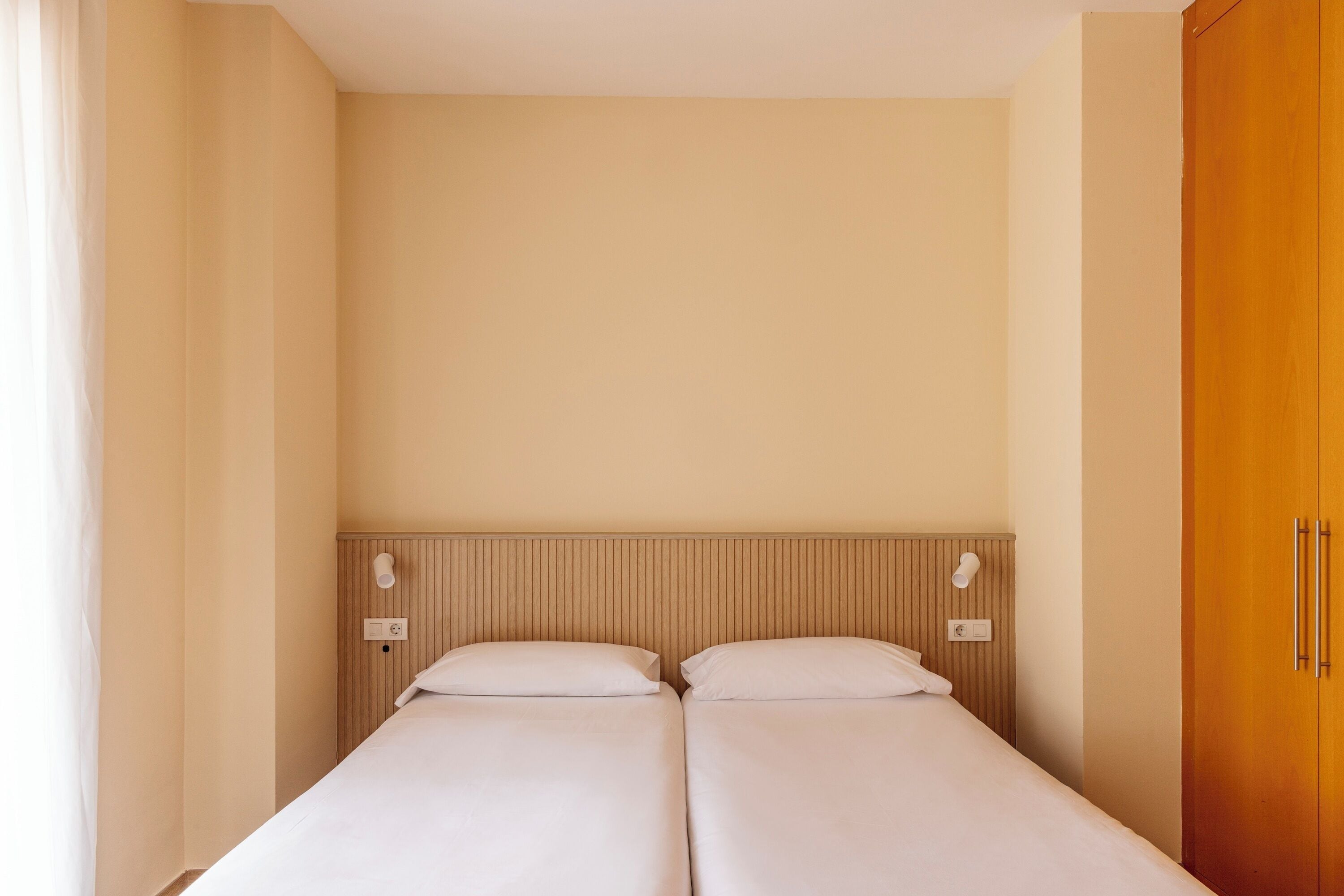 Uma cama de casal com cabeceira de madeira, duas mesas de cabeceira com luminárias e um guarda-roupa de madeira.