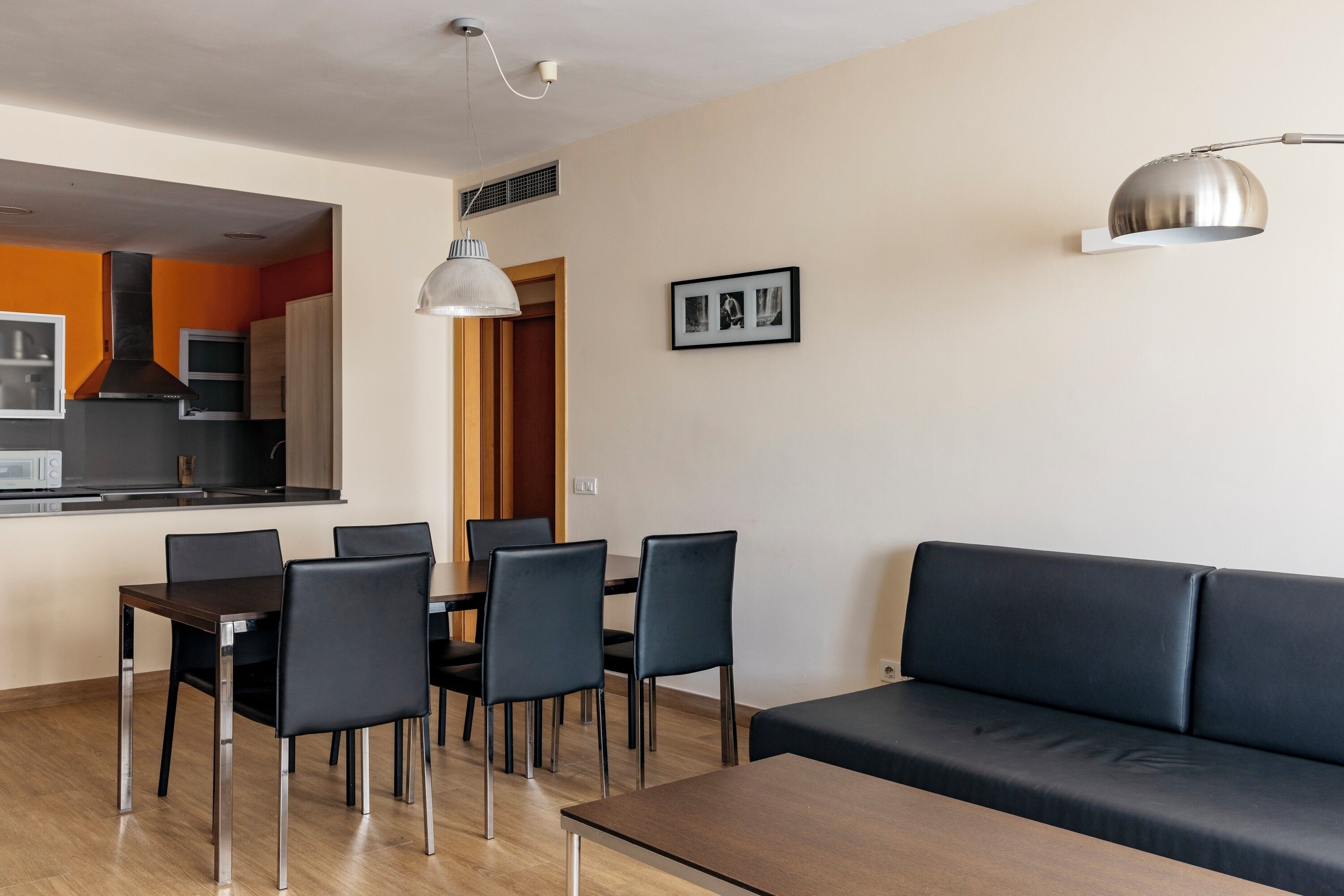 A modern living room with a sofa, dining table, chairs, and a kitchen area in the background.