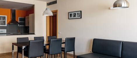 Una sala de estar moderna con sofá, mesa de comedor, sillas y una cocina al fondo.