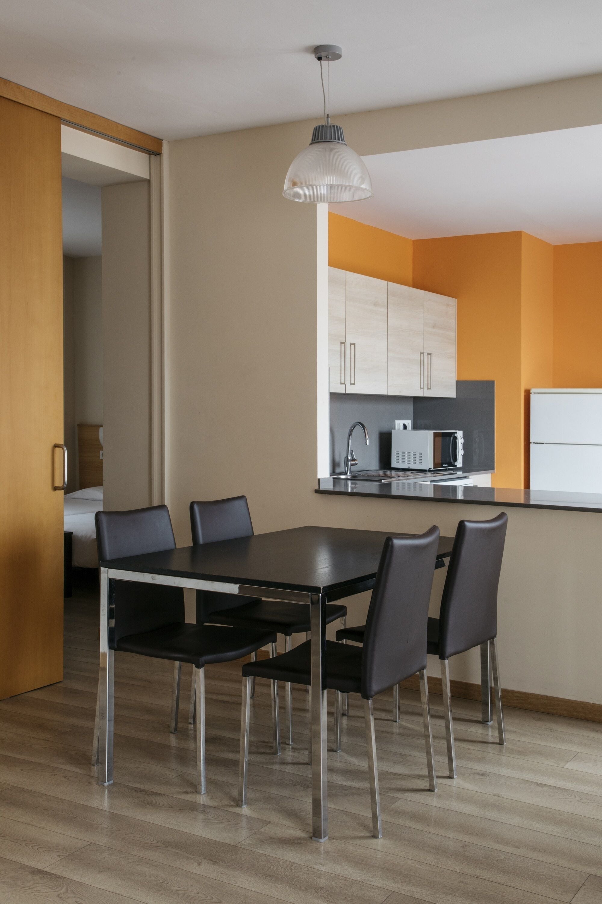 A modern kitchen with a dining area, featuring a black dining table with four chairs, a microwave, and a refrigerator.