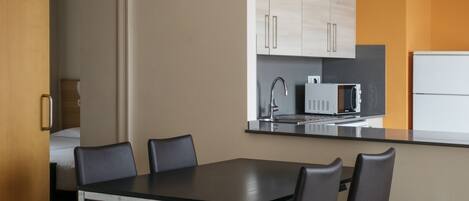 A modern kitchen with a dining area, featuring a black dining table with four chairs, a microwave, and a refrigerator.