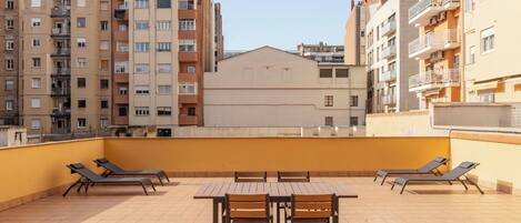 Eine Dachterrasse mit Liegestühlen und einem Tisch, umgeben von Hochhäusern.