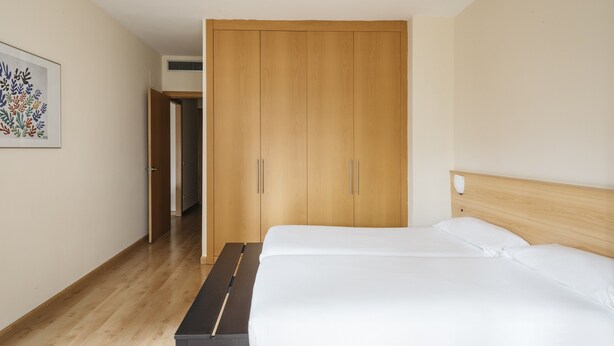 A bedroom with a wooden wardrobe, a bed with white bedding, and a wooden floor. - Villarroel Apartments Barcelona (Barcelona)