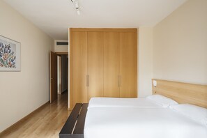 A bedroom with a wooden wardrobe, a bed with white bedding, and a wooden floor. - Villarroel Apartments Barcelona (Barcelona)