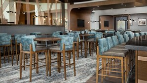 A modern restaurant with high tables and bar seating, wooden chairs, and contemporary lighting fixtures.