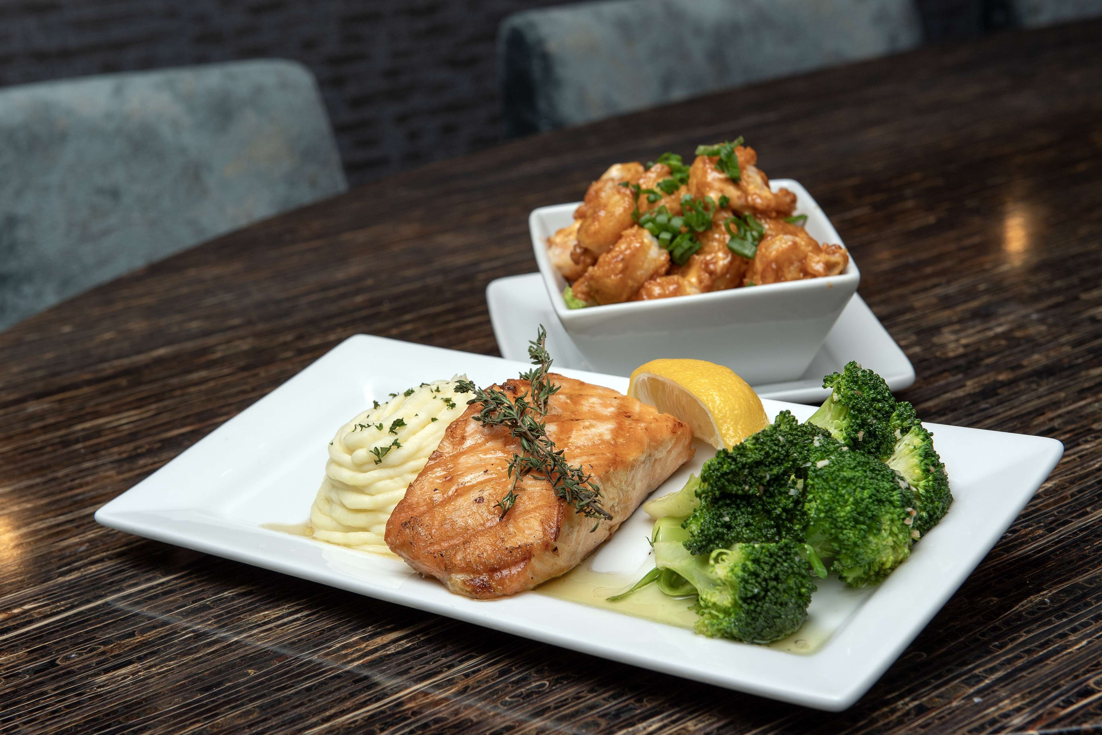 A plate of food with salmon, mashed potatoes, broccoli, and a lemon wedge.