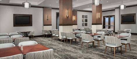 Un salón de conferencias de hotel con varias mesas y sillas, paneles de madera decorativos e iluminación empotrada en el techo.