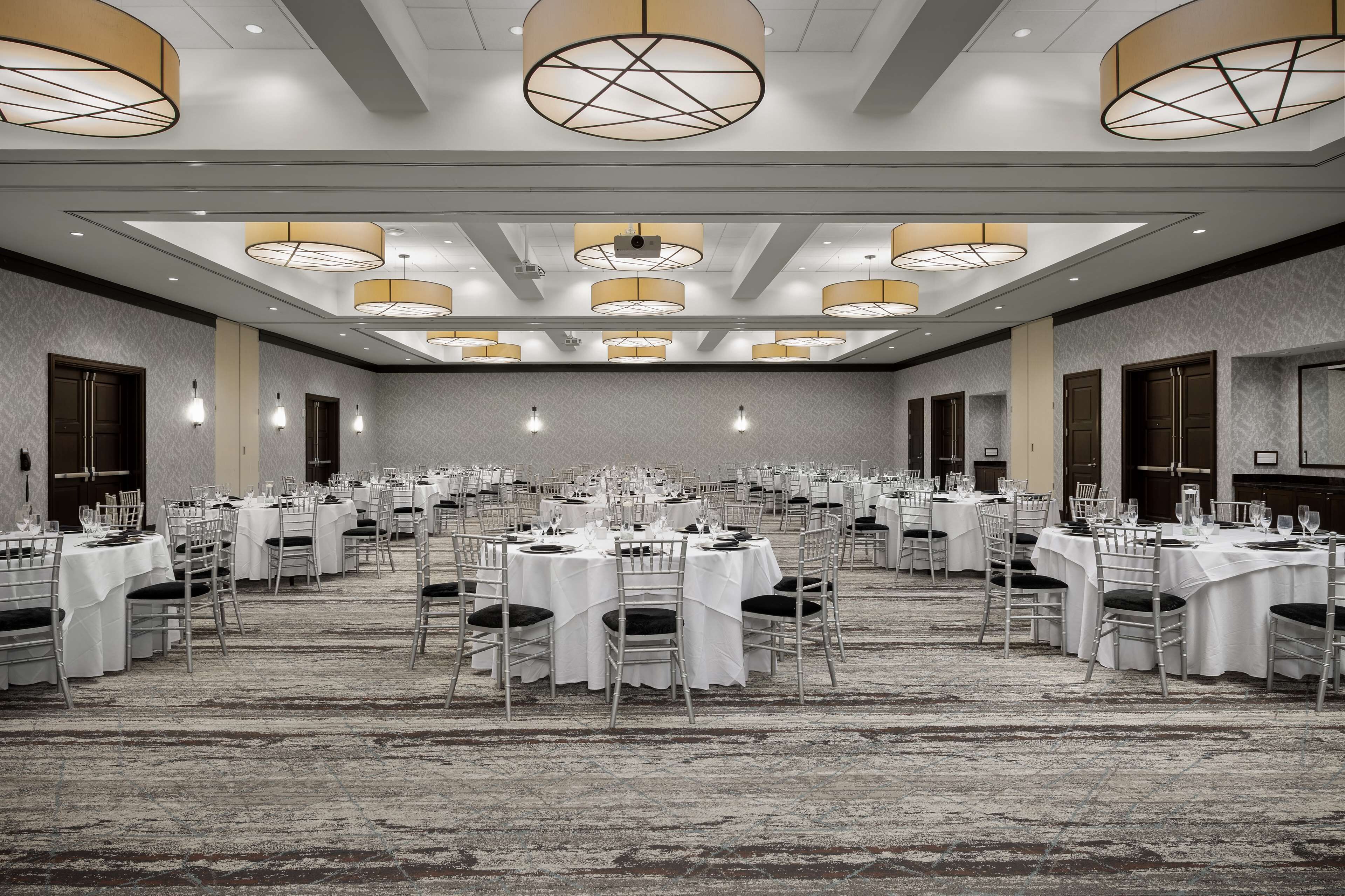 Un amplio salón de banquetes con varias mesas redondas dispuestas para comer, equipado con sillas y cubertería.