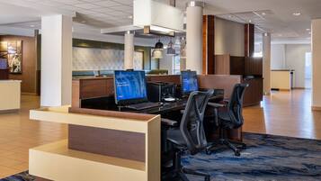 A modern hotel lobby with a reception desk, multiple computer workstations, and a large seating area.