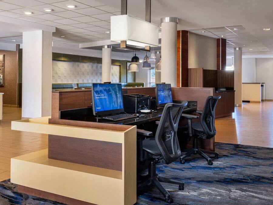 A modern hotel lobby with a reception desk, multiple computer workstations, and a large seating area.