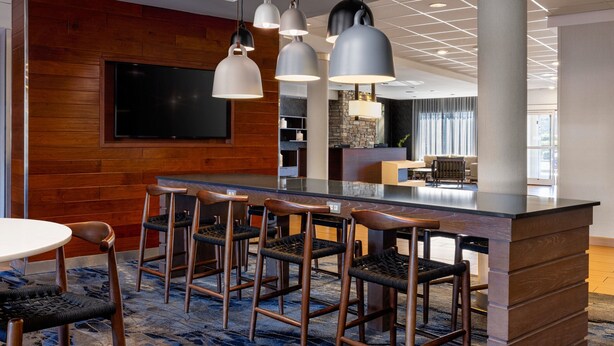 Een moderne bar met een wand van hout, een flatscreen televisie en een zithoek met barstoelen.
