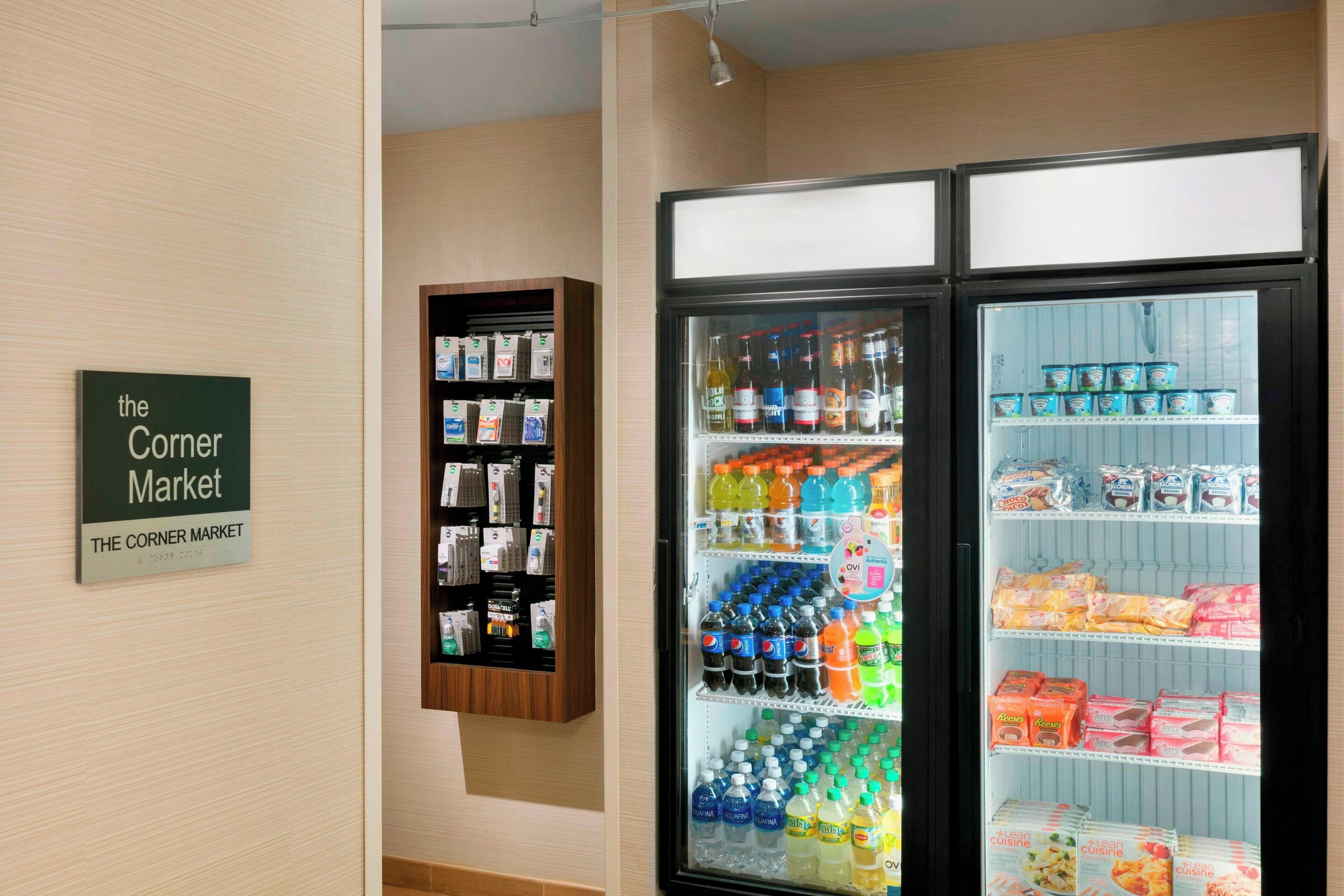 Une vitrine réfrigérée contenant des boissons et des produits emballés, une enseigne indiquant « The Corner Market », et une étagère avec divers articles.