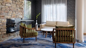 Een moderne woonkamer met een stenen openhaard, een beige bank en twee houten stoelen met groene kussens.